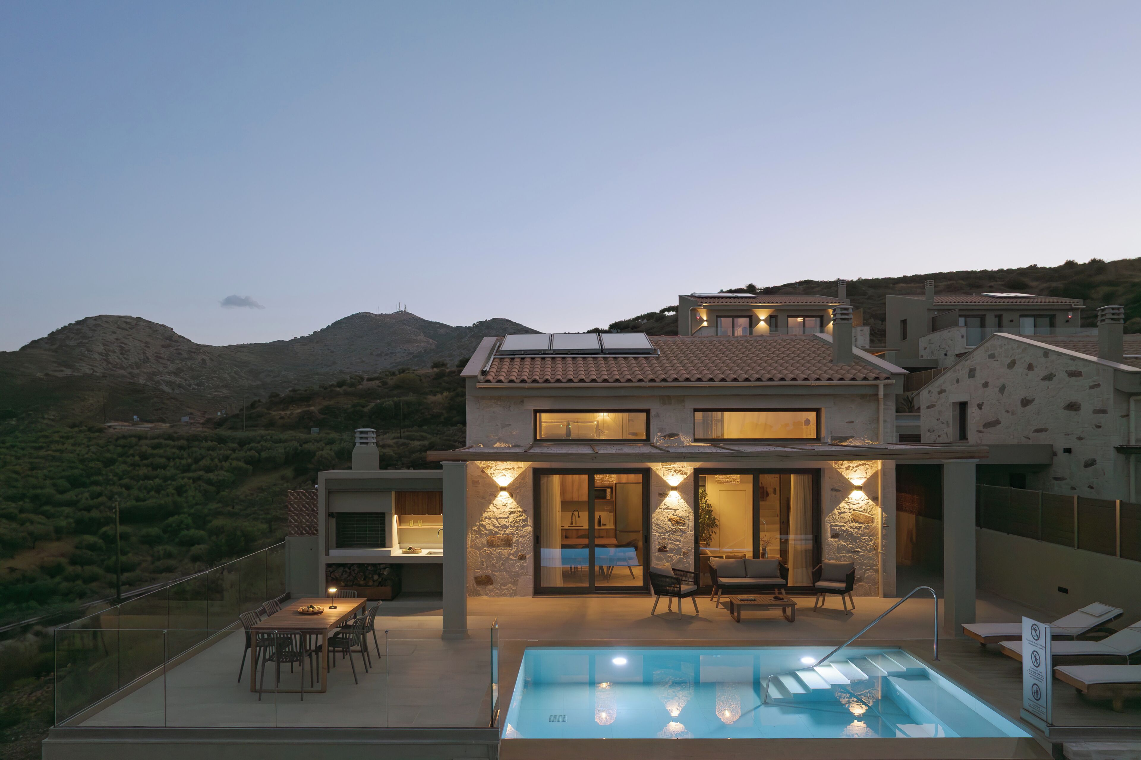 A modern house with a swimming pool, outdoor seating, and a view of the hills.