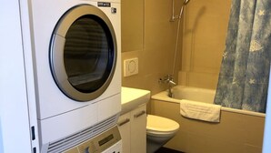 Un baño pequeño con lavadora y secadora apiladas, inodoro y ducha.