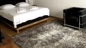 Una habitación de hotel con una cama, un sillón de cuero negro, un tapete estampado y una obra de arte en la pared.