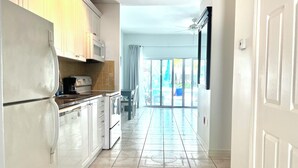 A kitchen with white cabinets, a refrigerator, and a microwave. There is a dining area with a table and chairs. The floor has patterned tiles.