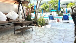 A poolside area with lounge chairs, a sofa, and a tiled floor.