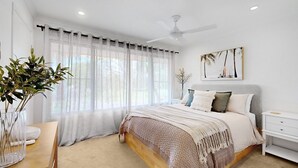 Ein Schlafzimmer mit Bett, Nachttisch, Deckenventilator und Fenster mit transparenten Vorhängen.