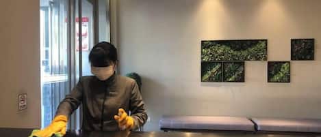 A person cleaning a reception desk in a hotel lobby with a bench and artwork on the wall.