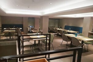 Un comedor moderno con varias mesas y sillas, un techo alto con iluminación empotrada y vistas al exterior.