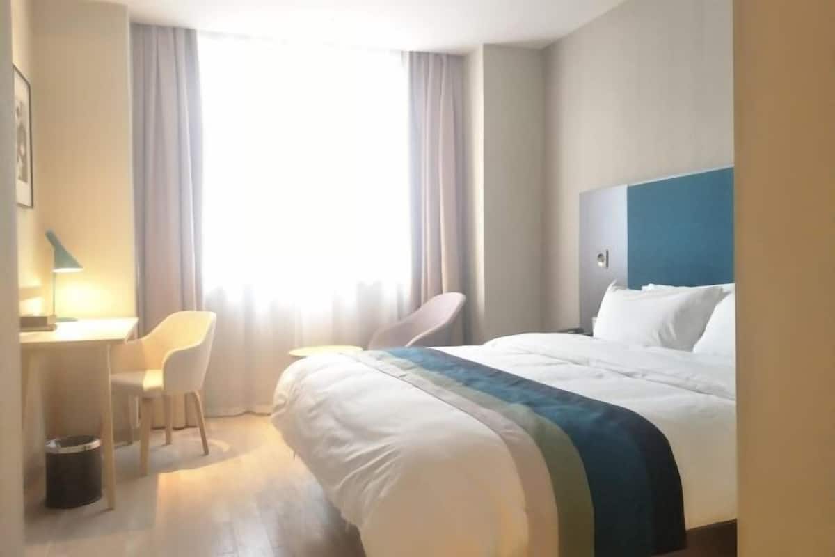 A hotel room with a bed, a desk, a chair, and a window with curtains.