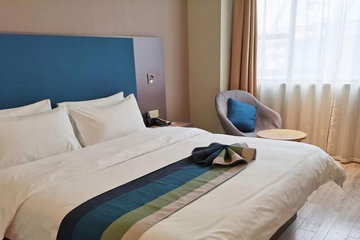 A hotel room with a bed, a chair, a small table, and a window with curtains.