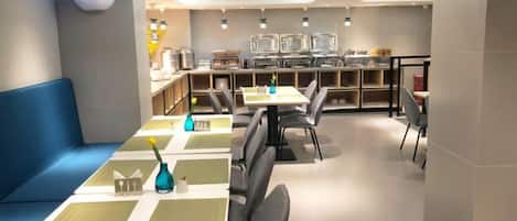 A modern restaurant with a long counter, blue seating, and a kitchen in the background.