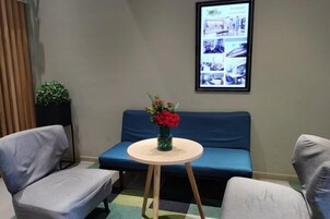 Una habitación con un sofá azul, una mesa redonda con un florero y un cuadro en la pared.