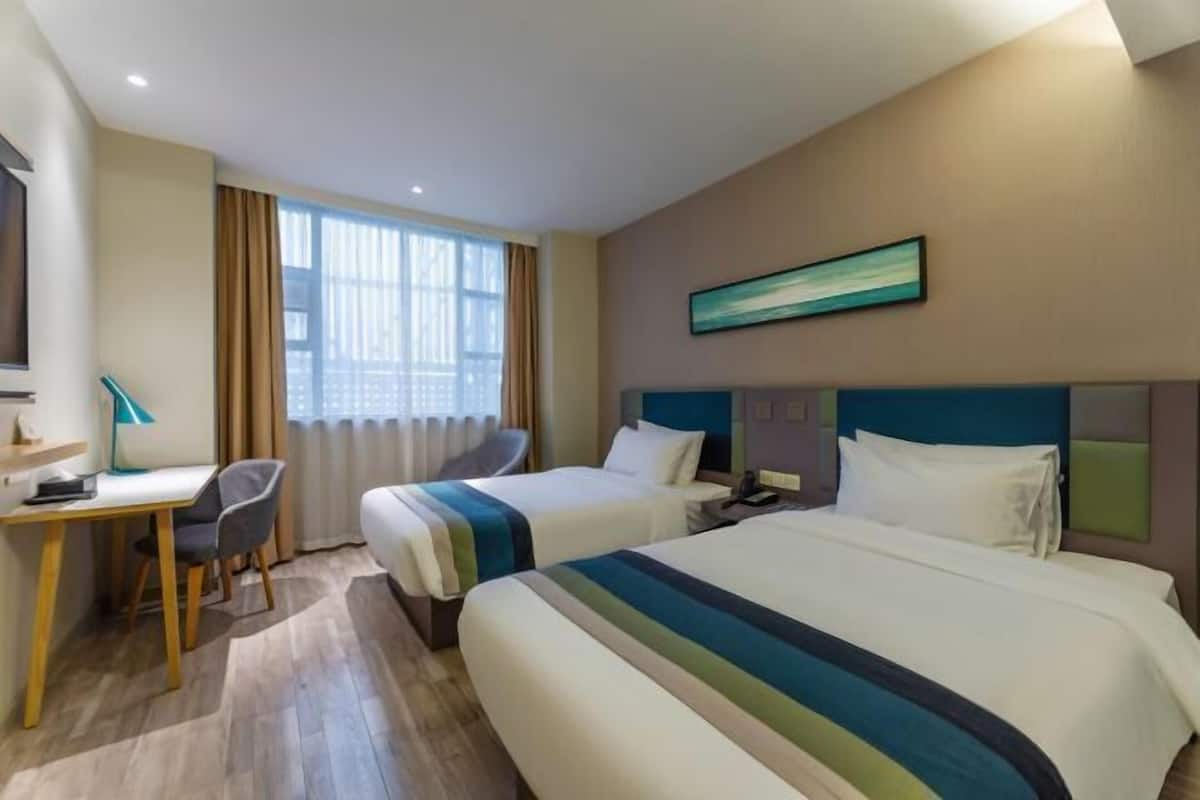 A hotel room with two beds, a desk, a chair, and a window with curtains.