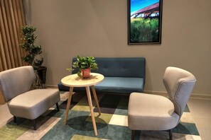 A room with a sofa, two armchairs, a small round table with a plant, and a painting on the wall.
