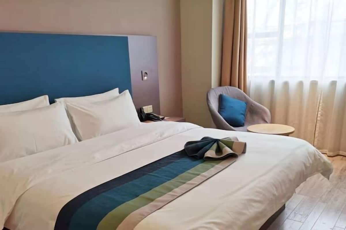 A hotel room with a bed, a chair, a small table, and a window with curtains.