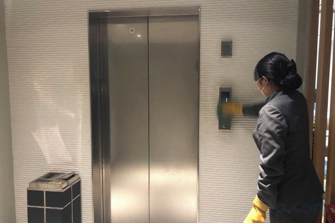 A person standing next to a metallic elevator in a room with a tiled wall.