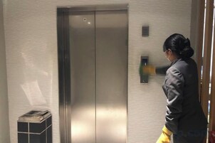 Una persona de pie junto a un ascensor metálico en una habitación con pared de azulejos.