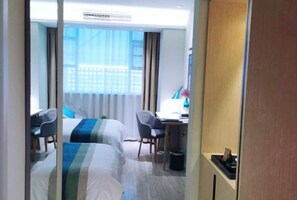 A hotel room with two beds, a desk, a chair, and a window with curtains.