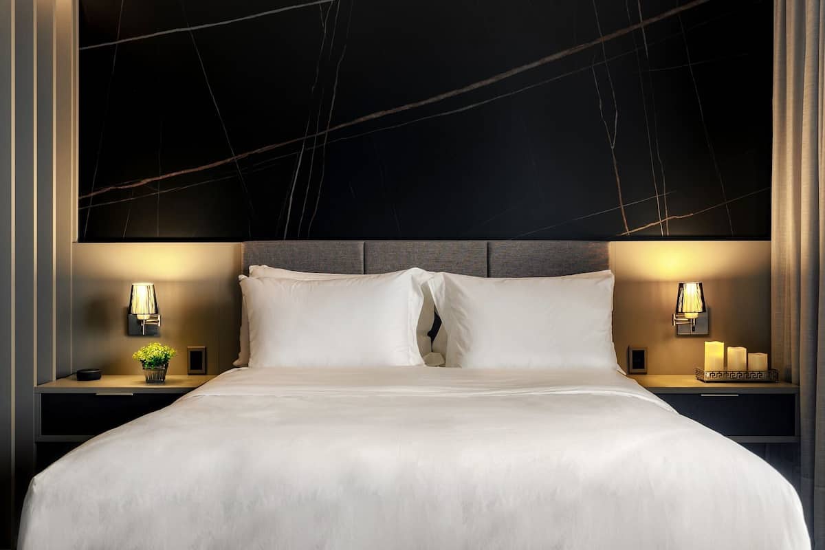 A modern hotel room with a large bed, two bedside tables with lamps, and a dark headboard with a marble-like design.