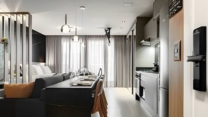 Et moderne køkken med rustfrie hvidevarer, et spiseområde med en central ø, samt en opholdsstue med sofa og gardiner.