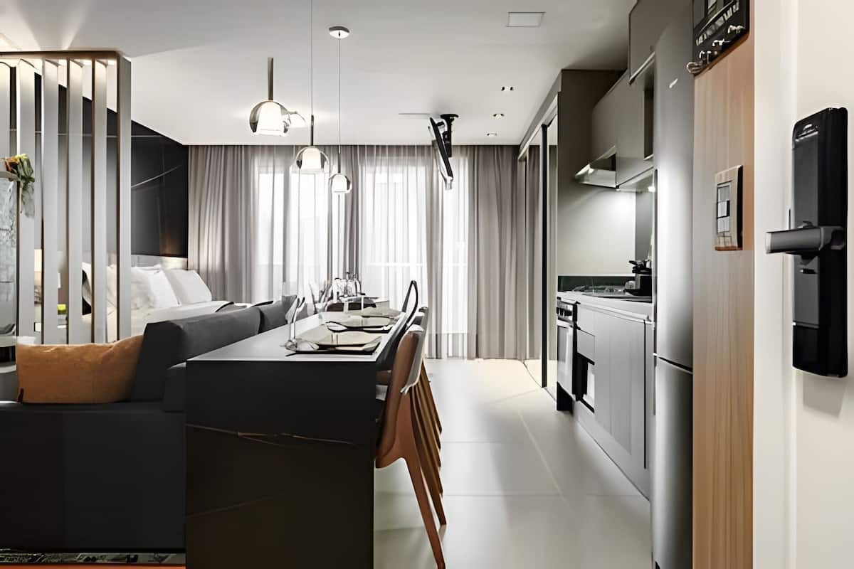 A modern kitchen with stainless steel appliances, a dining area with a central island, and a living space with a sofa and curtains.