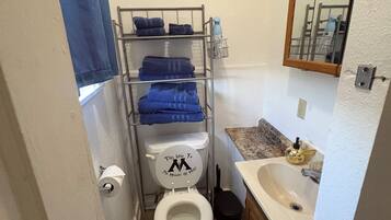 Casa de banho compacta com sanita, lavatório e espelho. Há um porta-toalhas com toalhas dobradas e uma toalha azul pendurada na parede.