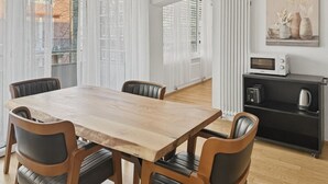 A dining area with a wooden table and chairs, a kitchen area with appliances, and a view through large windows. - Amazing 1BR flat in the city centre (West 8) (Zürich)