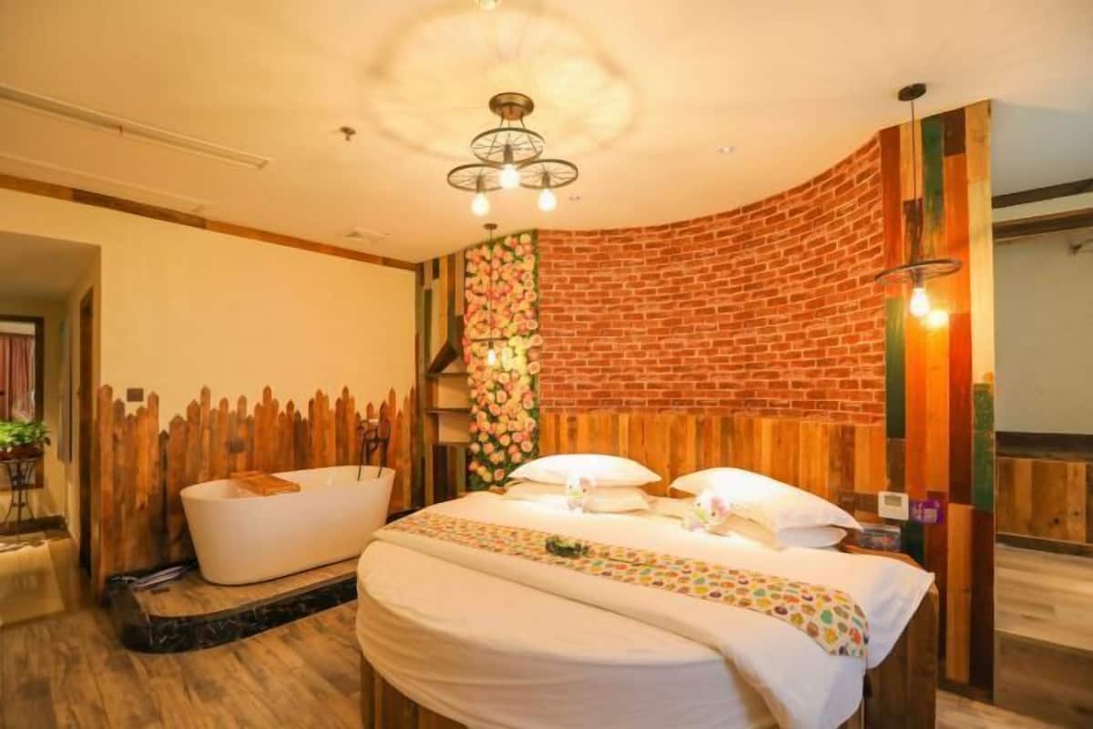 A modern hotel room with a brick accent wall, a large bed with white bedding, a wooden headboard, and a small bathtub.