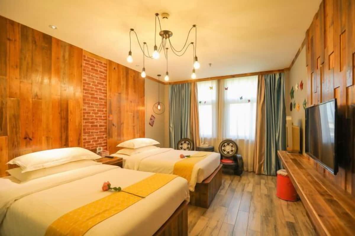 A hotel room with wooden walls, two beds, a TV, and a brick wall.
