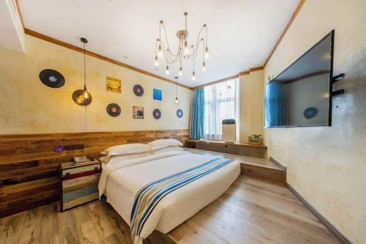 A bedroom with a bed, a chandelier, wall decor, a TV, and a window with curtains.