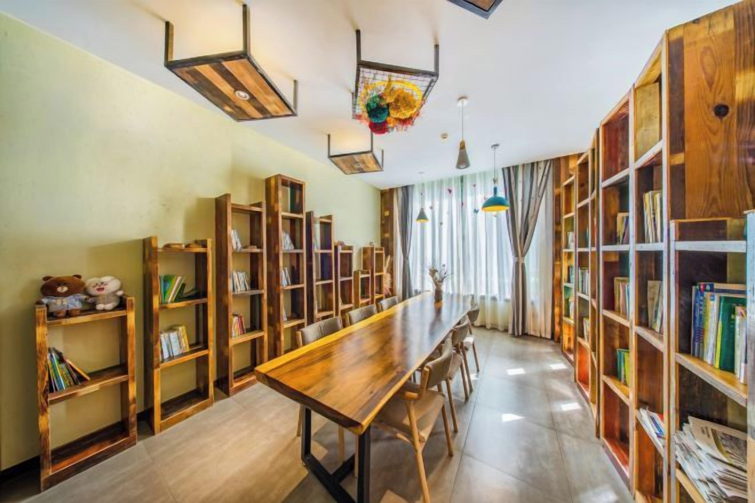 A room with a long wooden table, multiple bookshelves, and hanging light fixtures.