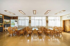 A conference room with a long table and chairs, large windows with curtains, and a wooden wall with shelves. - Shuiyue Qinghua Hotel (Deqing)