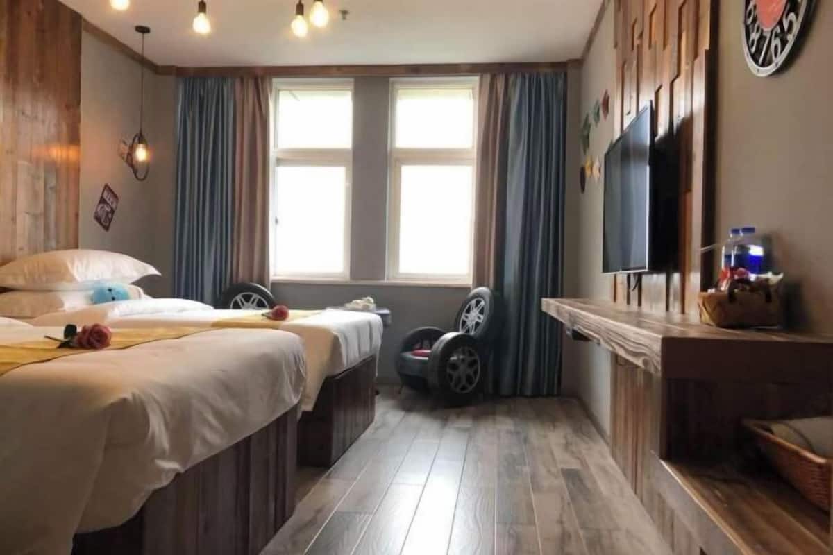 A room with two beds, a TV, a window with curtains, and a wall clock.