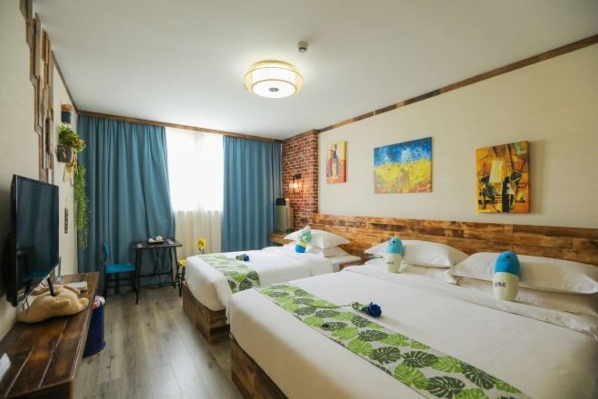 A hotel room with two beds, a desk, a TV, and artwork on the walls.
