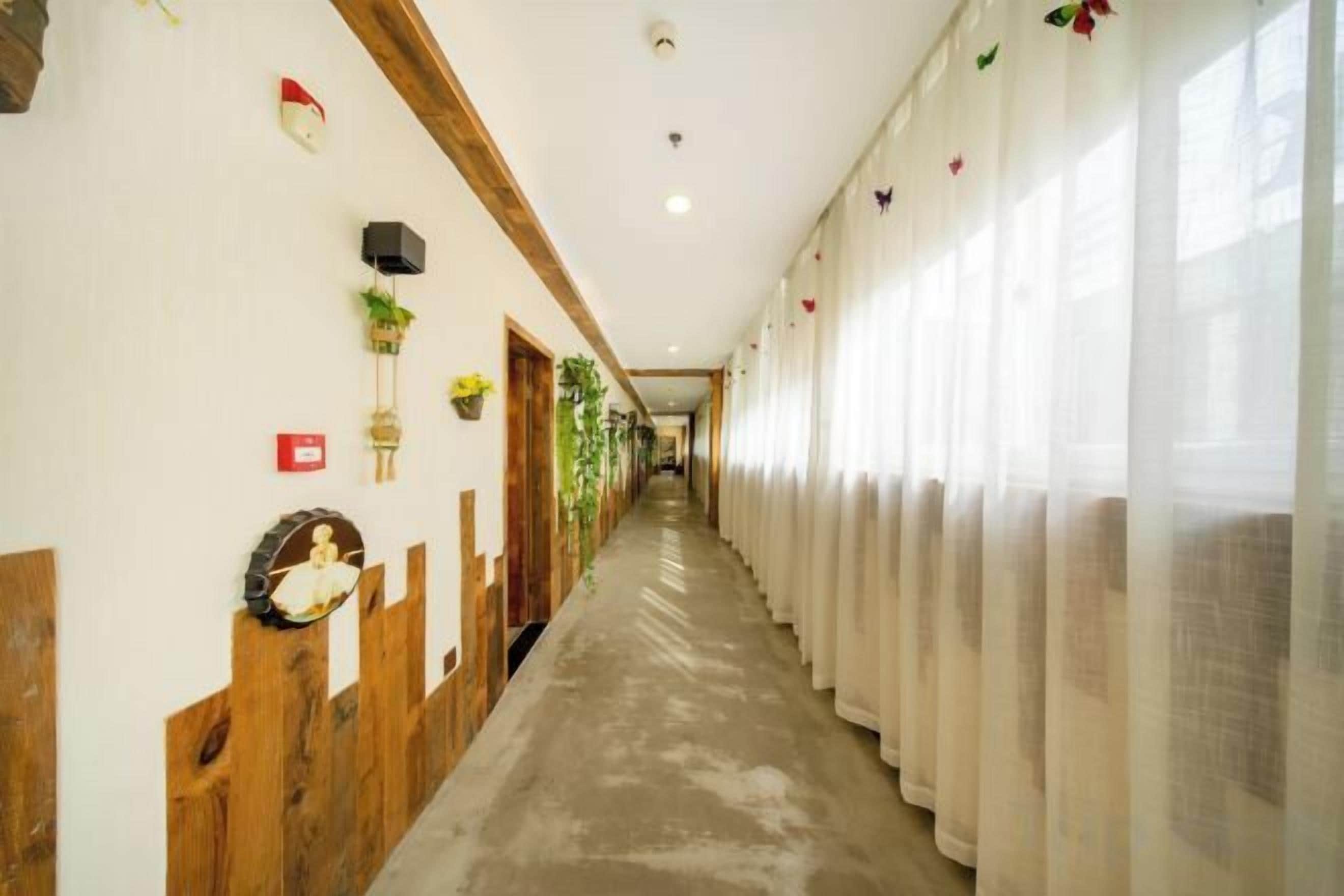 A hotel corridor with wooden paneling, a long hallway, and a row of windows with sheer curtains.