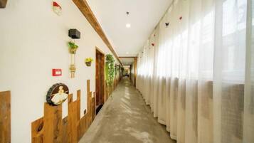 A hotel corridor with wooden paneling, a long hallway, and a row of windows with sheer curtains.