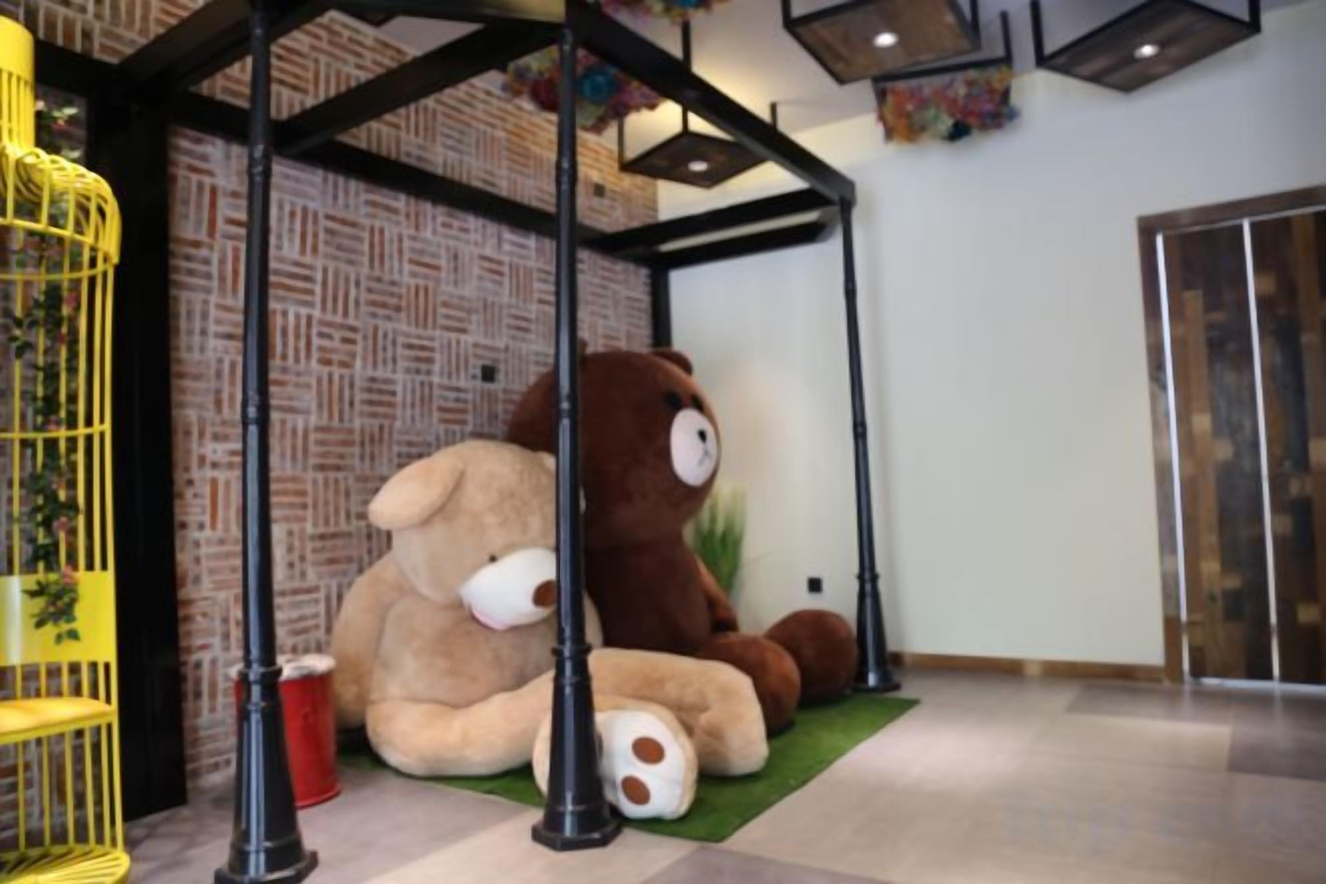 Un gran oso de peluche marrón sentado sobre una alfombra verde debajo de una estructura metálica negra.
