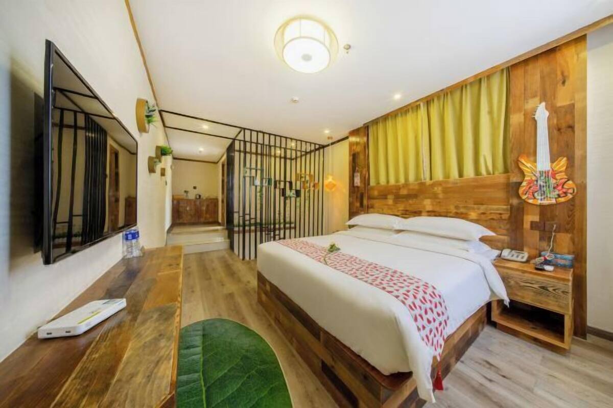 A bedroom with a bed, a desk, a chair, a guitar decoration, and a curtain.