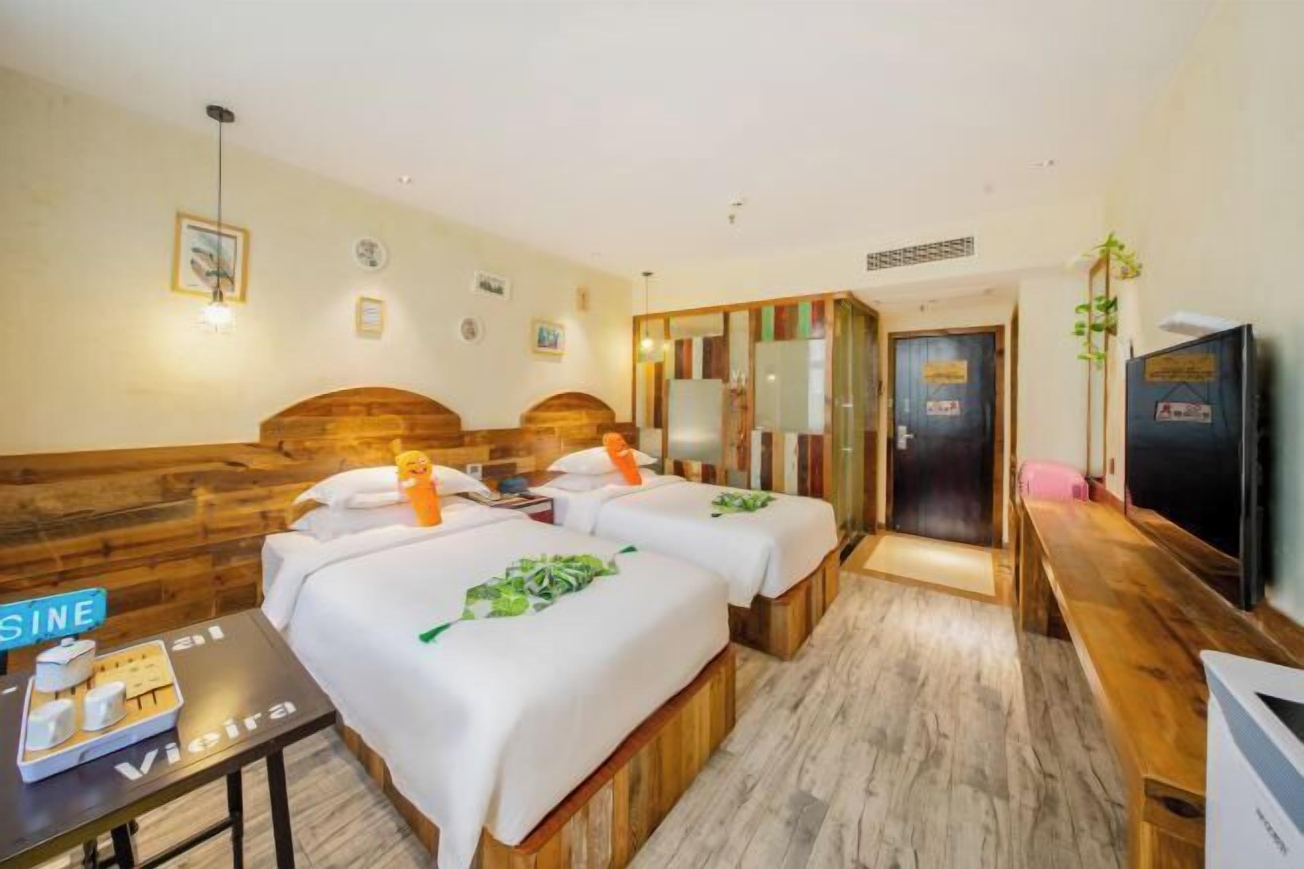 Habitación de hotel con dos camas, un banco de madera, una mesita con artículos de tocador y un televisor.