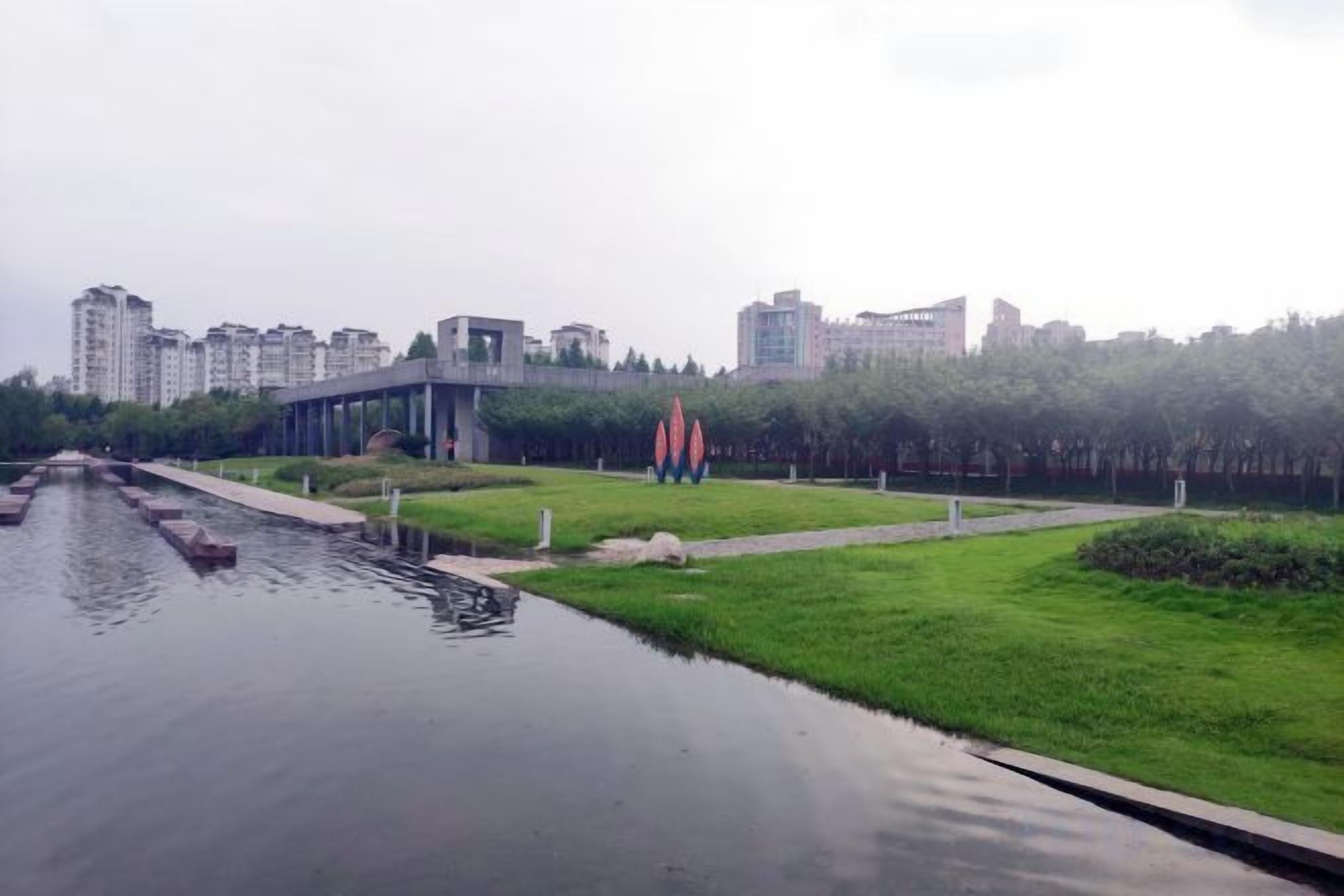 Un canal con un puente, una zona verde y esculturas rojas.