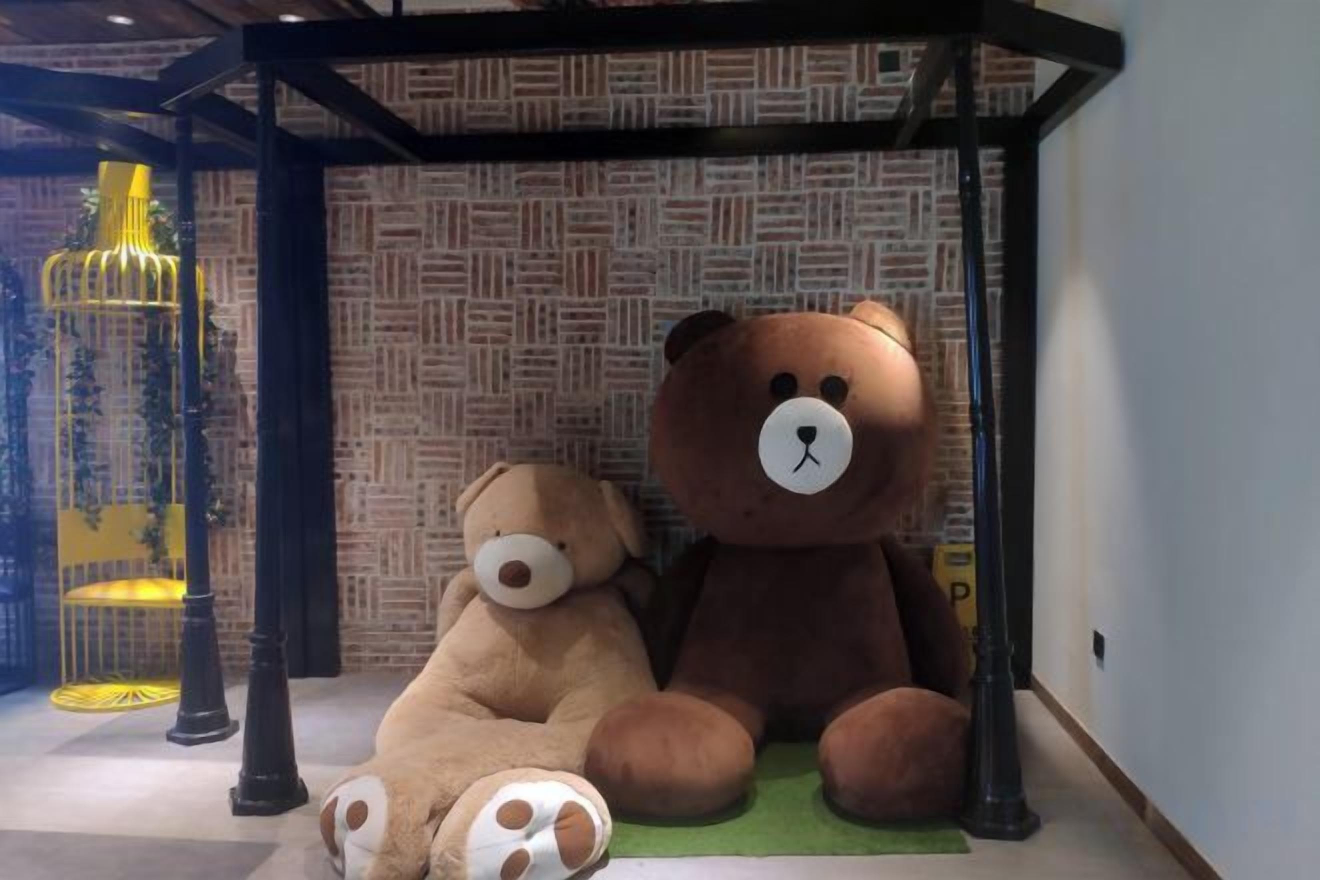A room with a patterned wall, a large teddy bear, and a yellow chair.