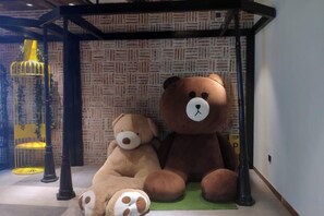 A room with a patterned wall, a large teddy bear, and a yellow chair. - Shuiyue Qinghua Hotel (Deqing)