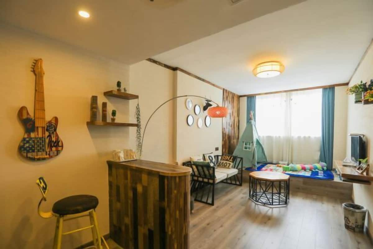 A room with a wooden bar, a guitar, a sofa, a dining table, and a window with curtains.