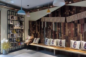 A cozy seating area with a wooden bench, plush cushions, and a shelf with various plush toys. - Shuiyue Qinghua Hotel (Deqing)