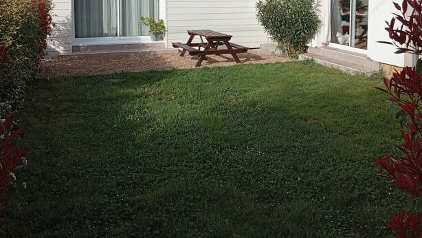 Une maison de plain-pied avec un toit en tuiles, une terrasse avec une table et des chaises, et une pelouse bien entretenue.