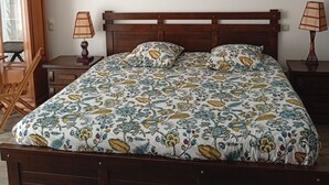 Une chambre à coucher avec un lit en bois, une literie à motifs floraux, deux lampes de chevet et un bureau en bois avec une chaise.