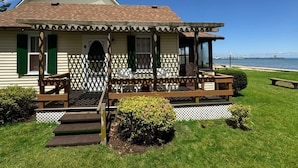 A coastal house with a wooden porch, steps leading to the entrance, and a view of the ocean. - Lake Cottage at Beachcomber of Mackinaw (Mackinaw City)