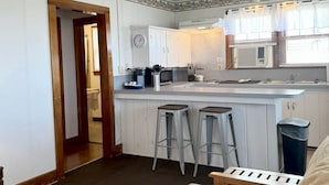 A compact kitchen with a central island, two bar stools, a ceiling fan, and a clock on the wall. - Lake Cottage at Beachcomber of Mackinaw (Mackinaw City)