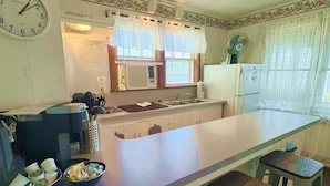 A kitchen with a central island, bar stools, a clock, and a refrigerator. - Lake Cottage at Beachcomber of Mackinaw (Mackinaw City)