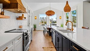 Une cuisine moderne avec des meubles blancs, un îlot central, une grande fenêtre et un luminaire suspendu.