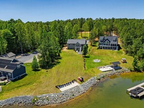 Una casa grande con un muelle y un bote pequeño, rodeada de un bosque.