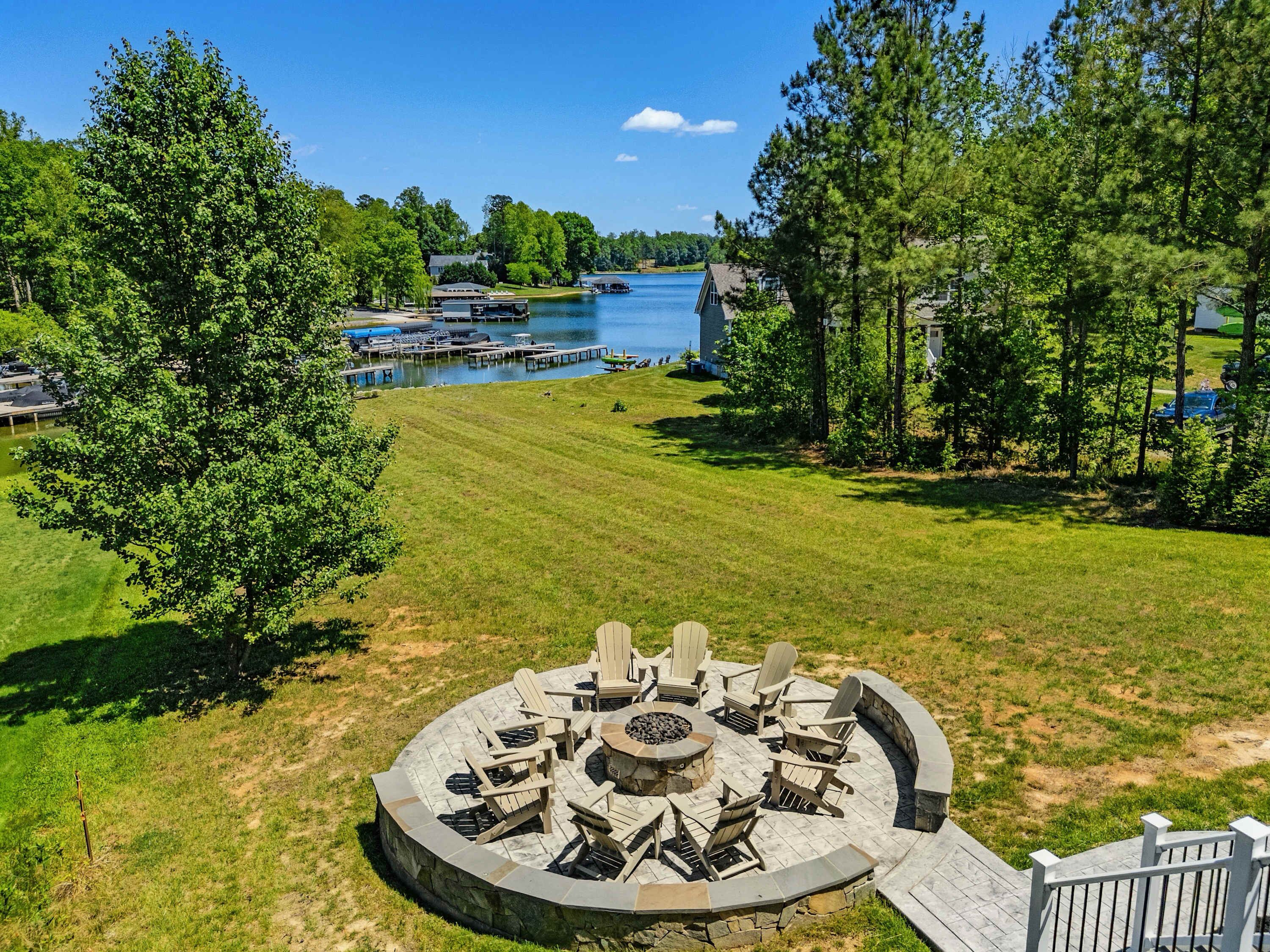 A circular outdoor seating area with Adirondack chairs and a fire pit, surrounded by a stone wall.