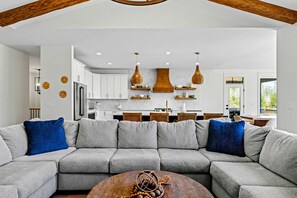 Un salon moderne avec un canapé d’angle, une table basse et une cuisine en arrière-plan.