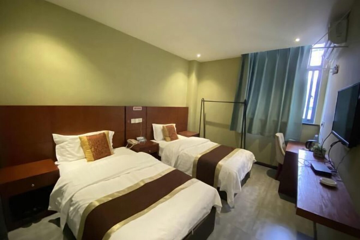 A hotel room with two beds, a desk, a chair, a TV, and a window with curtains.